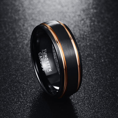 Black tungsten carbide ring with rose gold accent on a dark textured background