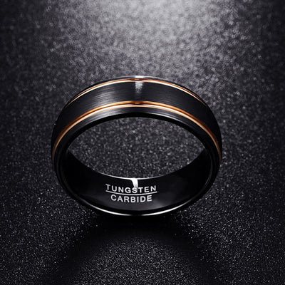 Black tungsten carbide ring with rose gold accents on a dark textured background