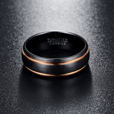 Black tungsten carbide ring with rose gold accents on a dark textured background