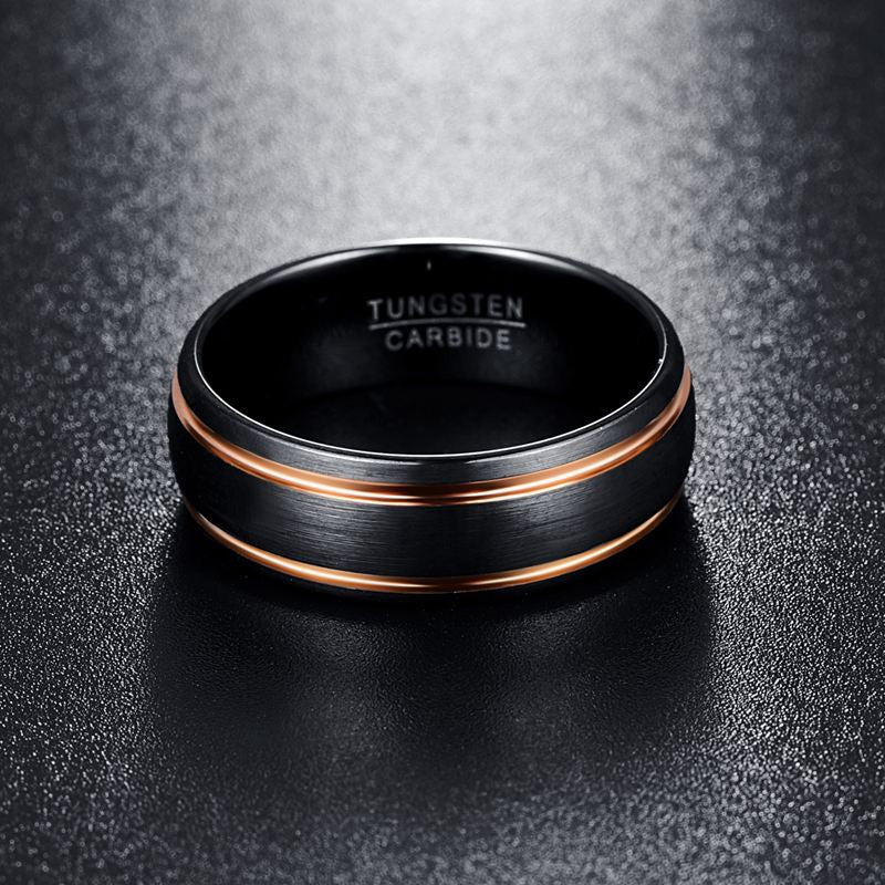 Black tungsten carbide ring with rose gold accents on a dark textured background